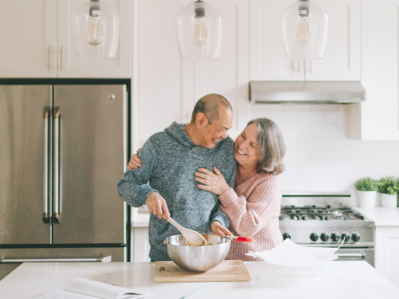 Senior couple smiling and laughing as they cook together.